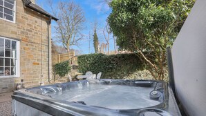 A hot tub in a backyard with stone walls and a wooden staircase.