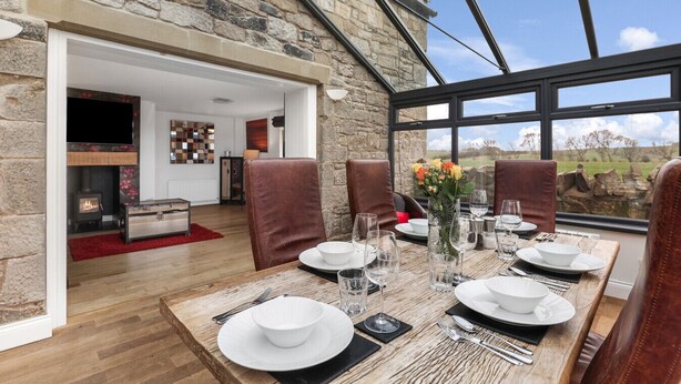 Un comedor con pared de piedra, mesa de madera y sillas de cuero.