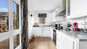 Una cocina moderna con armarios blancos, suelo de madera y vistas a un edificio de piedra.
