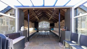 Un espacio de estar al aire libre con techo, paredes de piedra, una mesa y sillas.