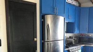 A kitchen with blue cabinets, a stainless steel refrigerator, a stove, and a microwave. - Byron's House At Secret Beach. (San Pedro)