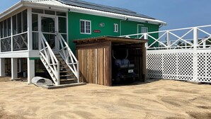 A green building with a covered garage and a white fence. - Byron's House At Secret Beach. (San Pedro)