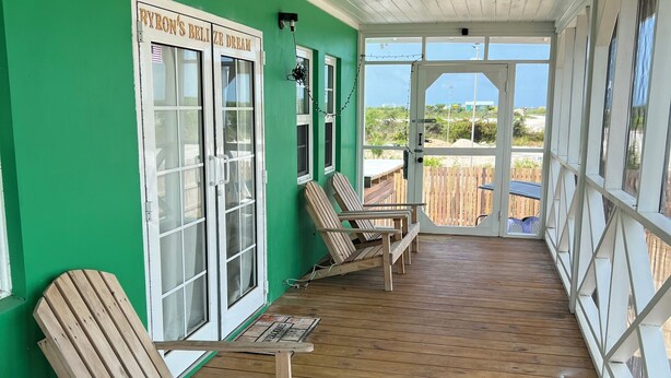 A covered porch with wooden chairs and a table, green walls, and a view of the beach. - Byron's House At Secret Beach. (San Pedro)