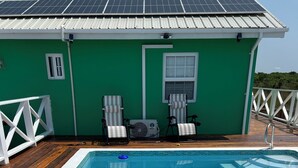 A rectangular swimming pool with a wooden deck, two lounge chairs, and a small fan. - Byron's House At Secret Beach. (San Pedro)