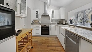 Une cuisine moderne avec des meubles blancs, un four encastré, une hotte en acier inoxydable et un meuble à vin en bois.