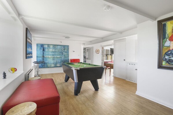 A spacious room with a pool table, a red bench, and a large abstract painting on the wall.