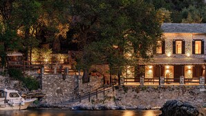 A stone building with a stone staircase leading up to a wooden deck overlooking a body of water. - Cleopatra's Miramare (Zagora-Mouresi)