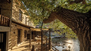 A stone building with a balcony overlooking a river, featuring outdoor seating and a view of the water. - Cleopatra's Miramare (Zagora-Mouresi)