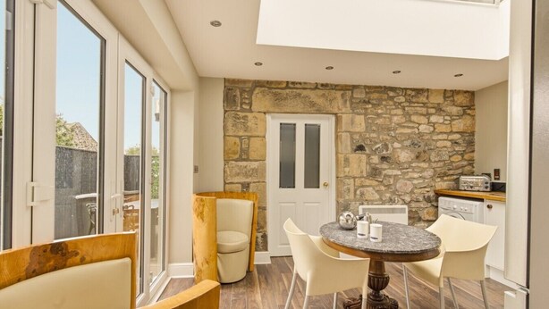 A modern kitchen with stone walls, a dining area with a round table, and a large window.