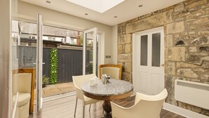 A room with a stone wall, a round table with chairs, a door, and a view of the outside.