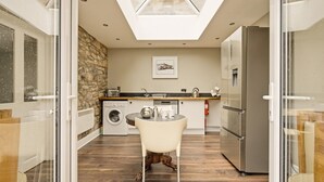 A modern kitchen with a stone wall, a washing machine, a sink, a refrigerator, and a skylight.