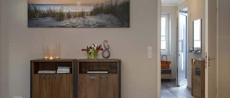 A hallway with a wooden console table, a painting of a beach scene, and a door leading to another room.