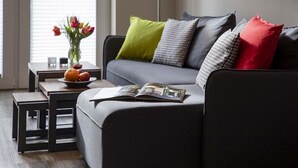 A modern living room with a grey sofa, a small table with a vase of flowers, and a magazine on the sofa.