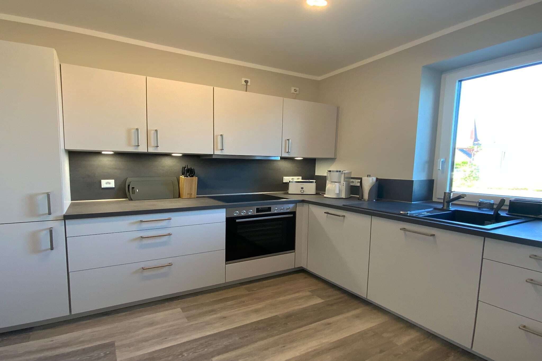 A modern kitchen with white cabinets, a built-in oven, and a window providing natural light.