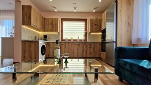 Een moderne keuken met houten kastjes, een eettafel met glazen blad en een zwarte bank.