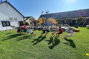 A group of children playing tug-of-war on a grassy field with playground equipment in the background.