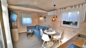 A cozy cabin with a wooden interior, a sofa, a dining table with chairs, a TV mounted on the wall, and a window with curtains. - Year-round, modern holiday home with a terrace (Ustronie Morskie)