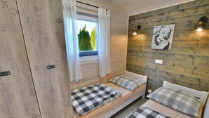 A small, cozy room with two beds, a window with curtains, and a wall-mounted light fixture. - Comfortable holiday home with a terrace, Ustronie (Ustronie Morskie)