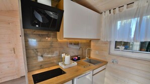 A compact kitchen with wooden walls, a built-in microwave, a sink, and a window with curtains. - Comfortable holiday home with a terrace, Ustronie (Ustronie Morskie)