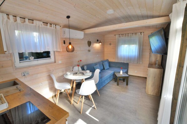 A cozy cabin interior with a dining area, a sofa, and a TV mounted on the wall.