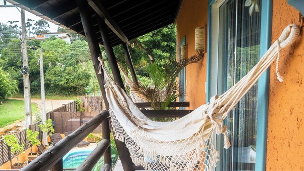 A hammock on a balcony with a view of a swimming pool and greenery. - Namaste Flats (Imbituba)