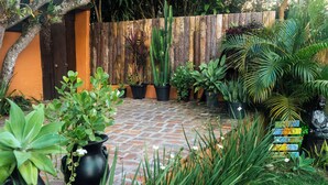 A garden with potted plants, a wooden fence, and a brick pathway. - Namaste Flats (Imbituba)