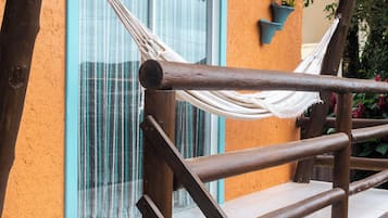 Un escalier en bois avec un hamac, une fenêtre aux bordures bleues et un pot de fleurs accroché au mur.