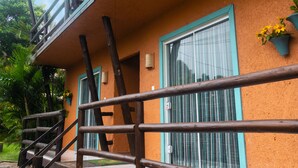 A two-story building with a balcony, a staircase, and a window with curtains. - Namaste Flats (Imbituba)