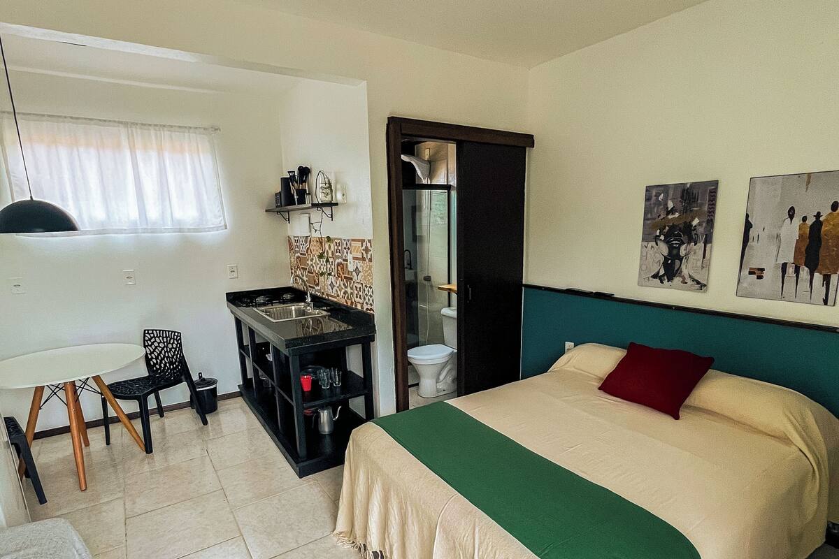 A bedroom with a bed, a desk, a chair, a ceiling fan, and a bathroom door.