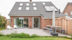 Una casa moderna con techo inclinado, amplios ventanales y terraza de madera.