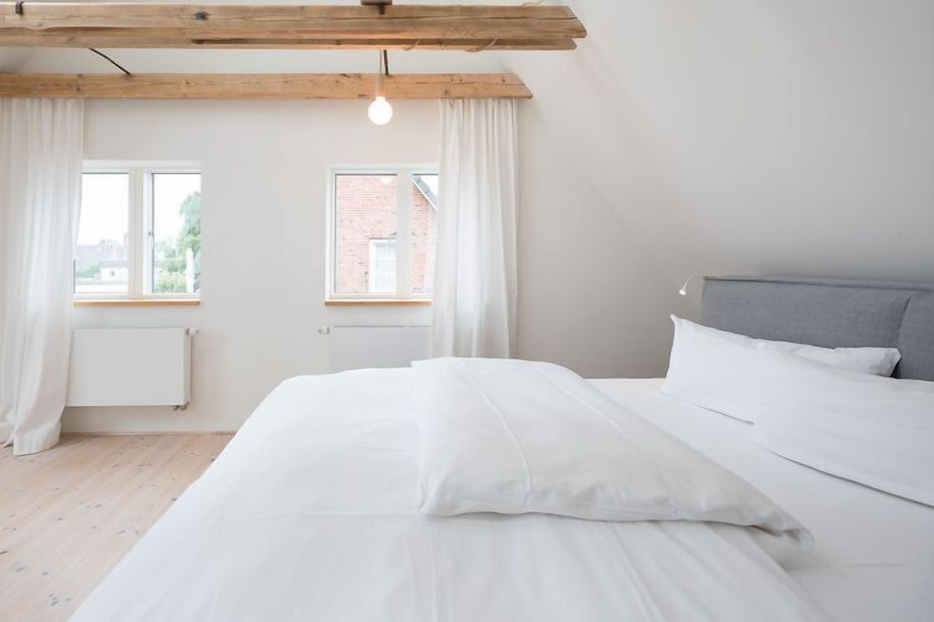 Ein Schlafzimmer mit Bett, Fenster, Heizkörper und einem Holzbalken an der Decke.