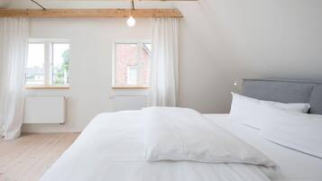 Ein Schlafzimmer mit Bett, Fenster, Heizkörper und einem Holzbalken an der Decke.