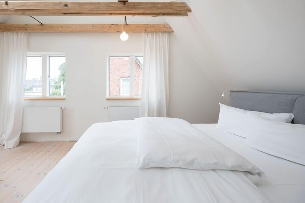 Une chambre à coucher avec un lit, une fenêtre, un radiateur et une poutre en bois au plafond.