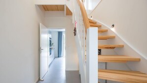 Una escalera moderna con escalones de madera y barandilla blanca, que conduce a una puerta abierta al final de un pasillo.