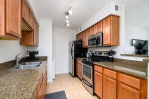 Una cocina con encimeras de granito, armarios de madera y electrodomésticos de acero inoxidable, incluyendo un microondas empotrado.