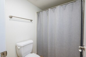A bathroom with a white toilet, a grey shower curtain, and a metal grab bar.