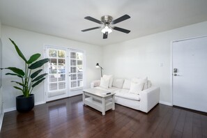 A room with a white sofa, a coffee table, a ceiling fan, and a potted plant.