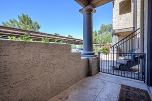 A covered outdoor area with a concrete wall, a metal railing, and a staircase leading to a building entrance.