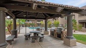 An outdoor patio with a grill and seating area, a pool in the background, and a covered pergola structure. - 2BR Gated Condo Near Old Town | Pool + Gym (Scottsdale)
