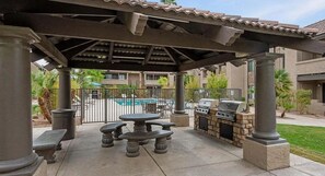 An outdoor patio with a grill and seating area, a pool in the background, and a covered pergola structure. - 2BR Gated Condo Near Old Town | Pool + Gym (Scottsdale)