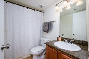 A bathroom with a white toilet, a shower curtain, a sink with a mirror, and a towel rack.