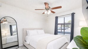 A bedroom with a bed, a ceiling fan, a window with blinds, and a large mirror. - 2BR Gated Condo Near Old Town | Pool + Gym (Scottsdale)