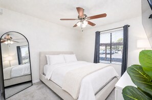 A bedroom with a bed, a ceiling fan, a window with blinds, and a large mirror. - 2BR Gated Condo Near Old Town | Pool + Gym (Scottsdale)