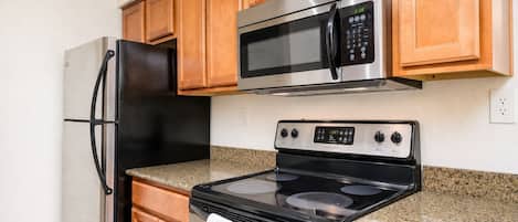 A kitchen with wooden cabinets, a stainless steel refrigerator, a microwave, and an oven.