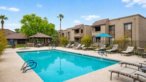 A swimming pool with lounge chairs and umbrellas, surrounded by buildings with a modern design. - 2BR Gated Condo Near Old Town | Pool + Gym (Scottsdale)
