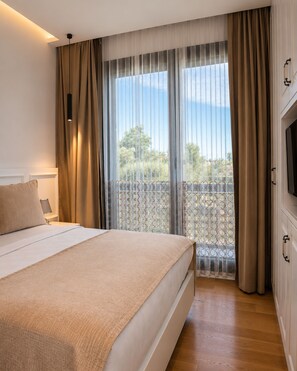 A bedroom with a bed, a TV, a window with curtains, and a balcony view. - CUNDA EYE (Ayvalik)