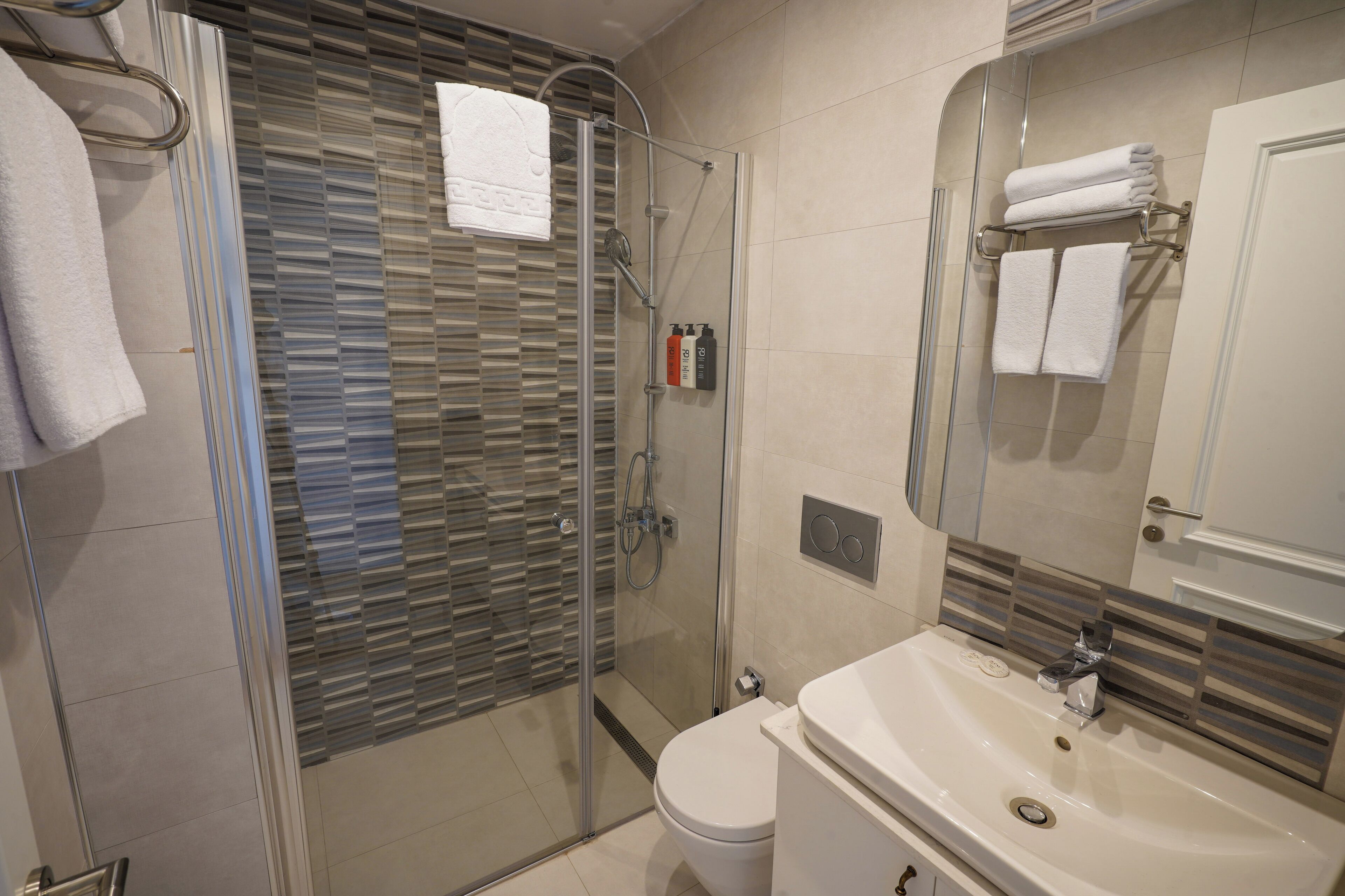 Une salle de bain moderne avec une douche à parois de verre, des toilettes blanches et un lavabo surmonté d’un miroir.