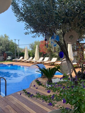 A swimming pool with lounge chairs, a wooden deck, and decorative elements like hanging baskets and a tree.