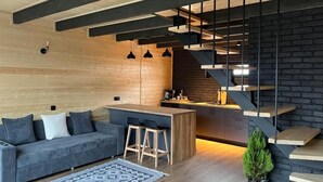 Una cucina moderna con un'isola centrale, una scala scura e un divano grigio con sgabelli da bar.