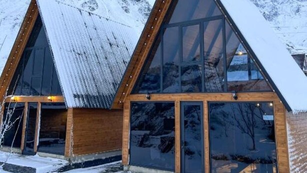 Un moderno chalet con ampie vetrate e struttura in legno, sullo sfondo di una montagna innevata.
